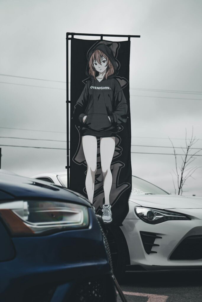 Anime-themed car display featuring a striking character banner between two parked cars.